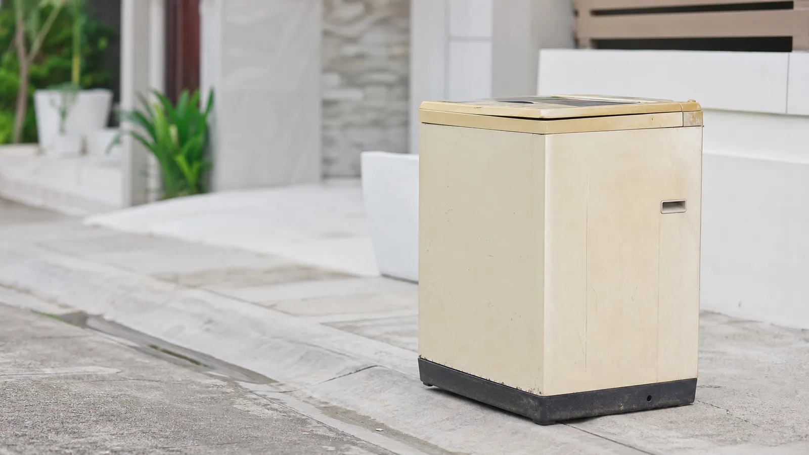 An old beige household appliance standing on the pavement outside a house awaiting collection