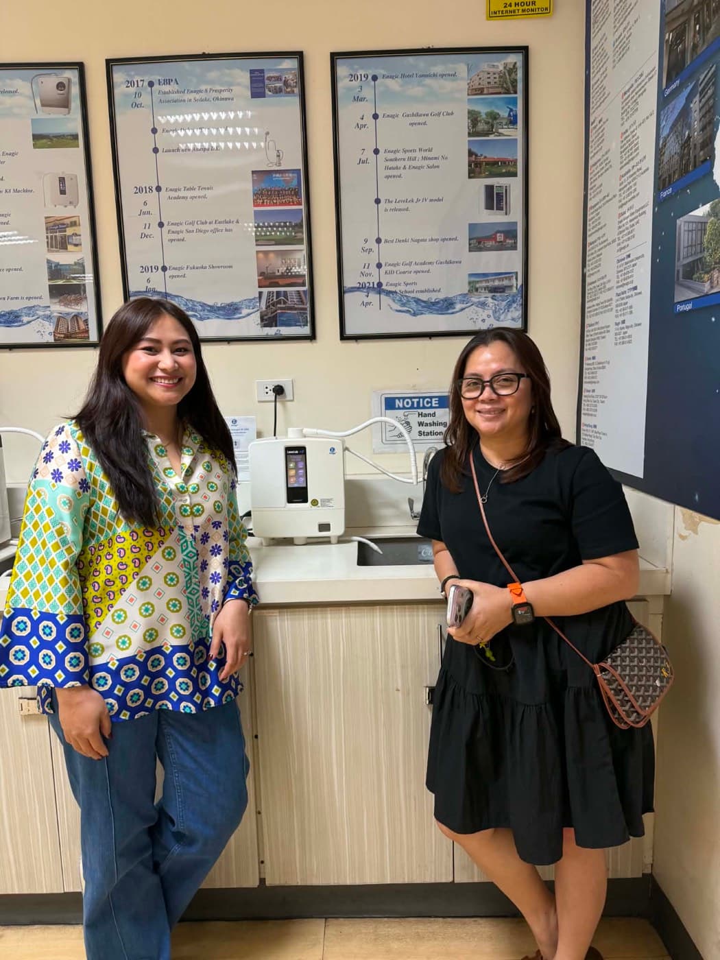 Two people beside a Leveluk K8 plumbed into a demonstration counter at an Enagic office