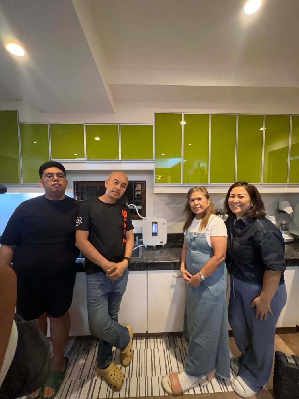 Four people in a kitchen with lime-green cabinets, beside a newly installed Leveluk K8